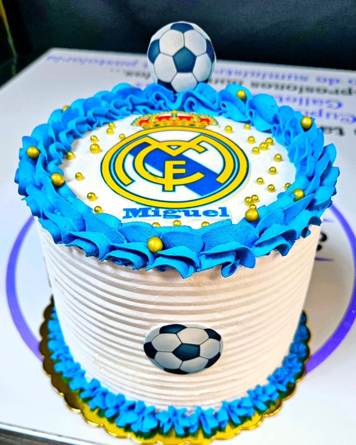 Un pastel blanco con glaseado azul y un balón de fútbol encima.