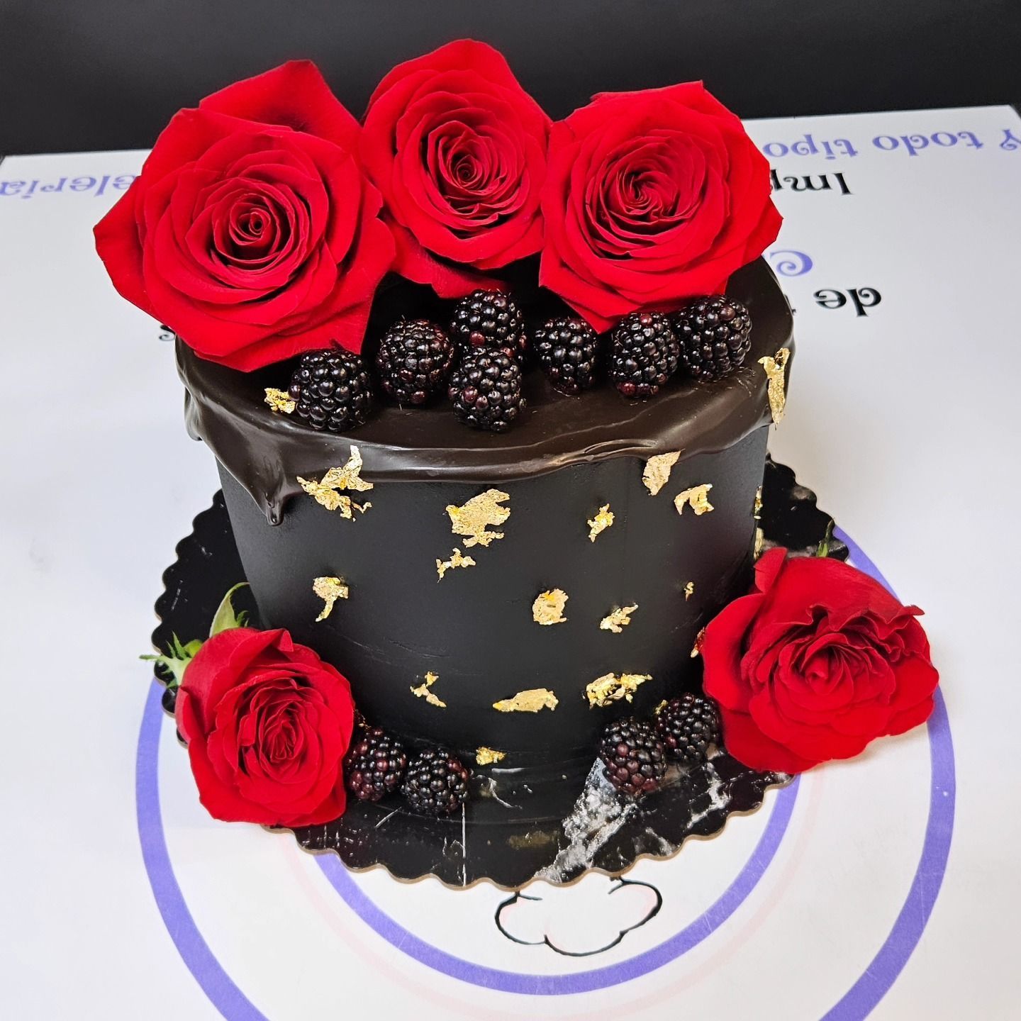 Un pastel de chocolate con rosas rojas y moras encima.