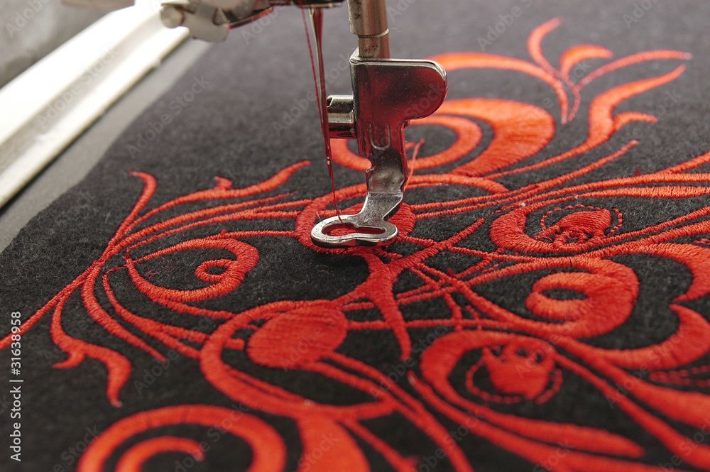 Eine Nähmaschine stickt ein rotes Muster auf einen schwarzen Stoff.