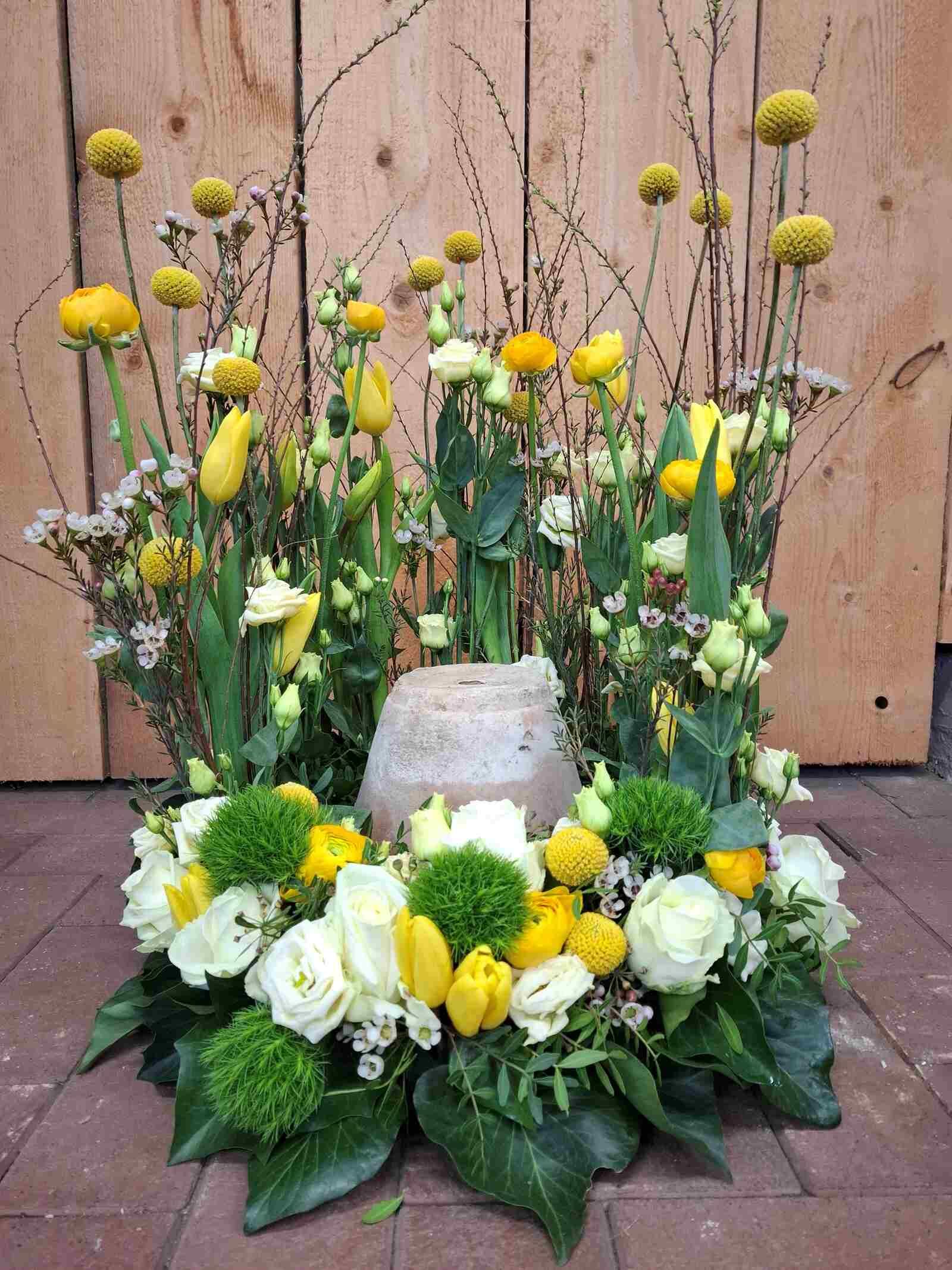 Auf einem Ziegelboden steht eine Vase mit gelben und weißen Blumen.