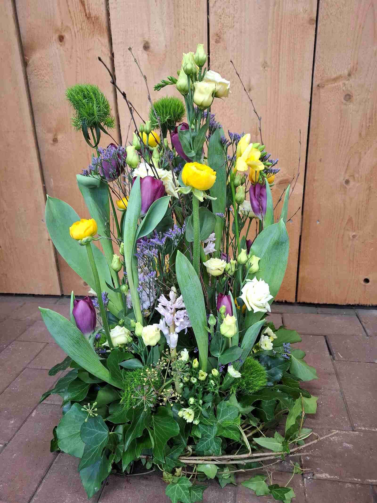Ein Blumenstrauß steht auf einem Ziegelboden vor einer Holzwand.
