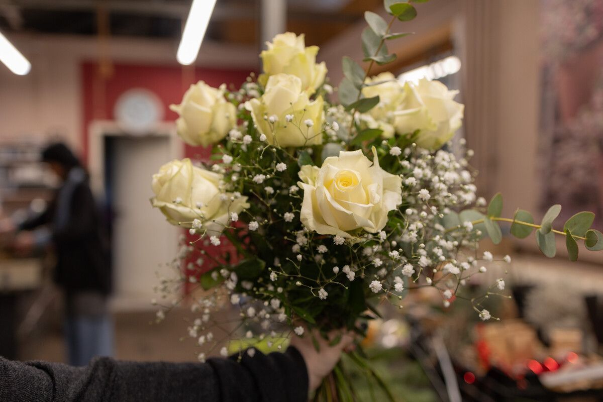 Eine Person hält einen Strauß weißer Rosen mit Schleierkraut in einer Vase.