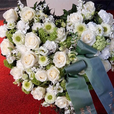 Ein herzförmiges Arrangement aus weißen Rosen und grünen Blumen mit einem blauen Band
