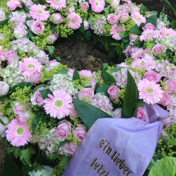 Ein Kranz aus rosa Blumen mit einem lila Band