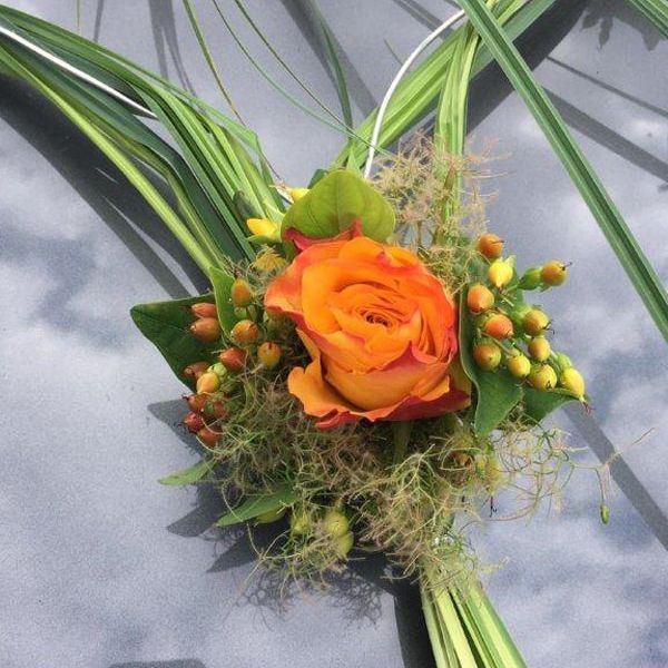 Eine orange Rose ist von Grün umgeben auf der Motorhaube eines Autos