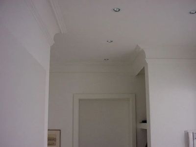 Weisse Decke mit Zierleisten und Einbauleuchten, die in eine Ecke über einem Türrahmen übergeht.