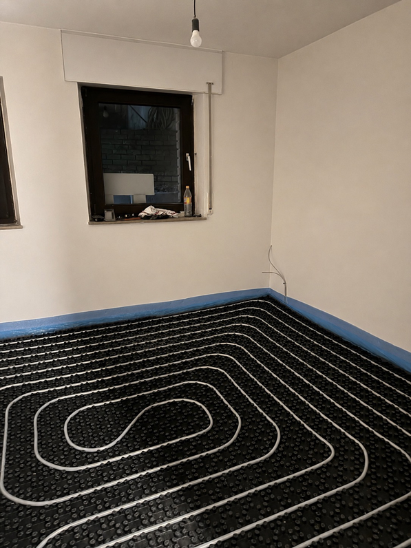 Leeres Zimmer mit schwarz-weiß gemustertem Bodenbelag, blauen Fußleisten und zwei Fenstern an einer weißen Wand.