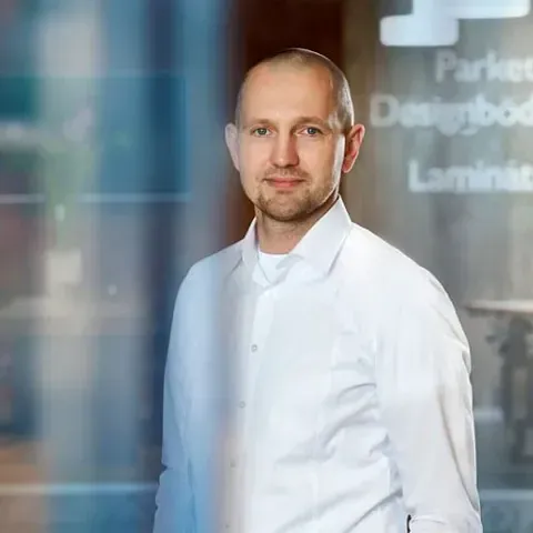 Mann in weißem Hemd steht drinnen vor einer verschwommenen Glaswand