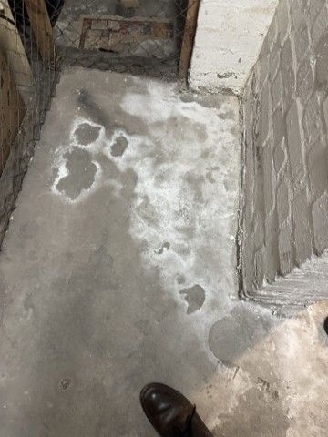 Betonboden mit nassen Stellen in der Nähe einer Ziegelwand und einem Schuh an der Unterkante