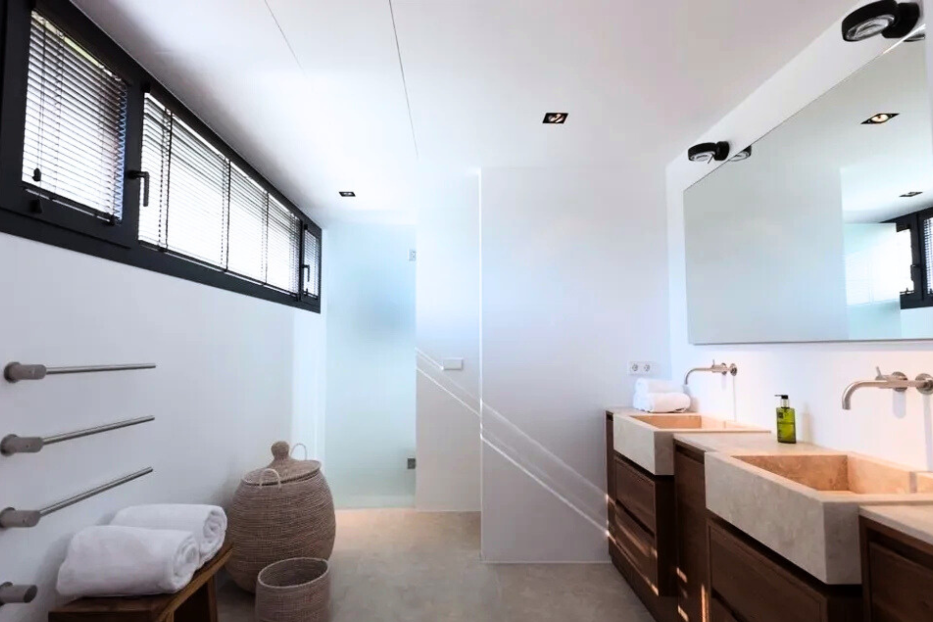 Baño blanco moderno con tocador de madera, lavabos de piedra y ducha de vidrio esmerilado.