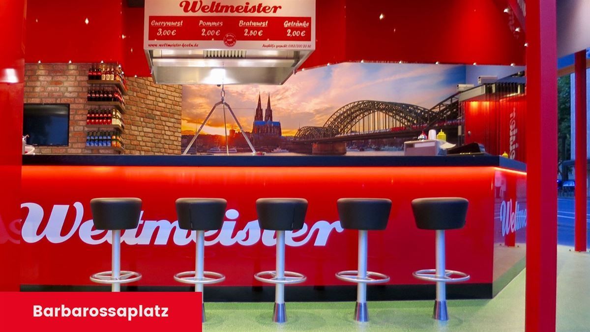 Eine rote Bar mit Hockern und einem Schild mit der Aufschrift „Barbarossaplatz“