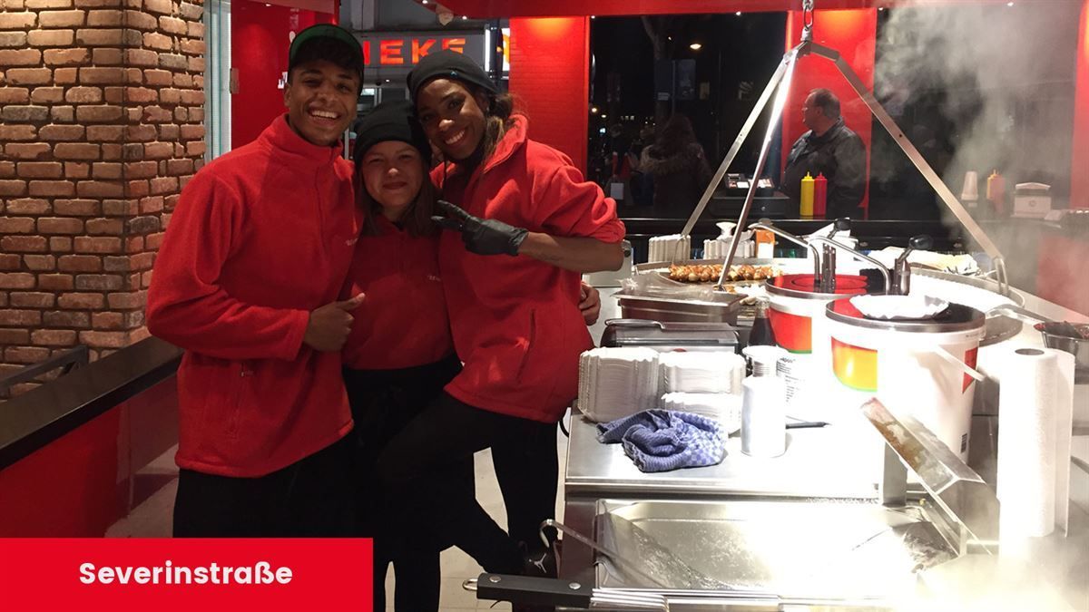 Eine Gruppe von Menschen posiert für ein Foto vor einem Schild mit der Aufschrift „Severinstrabe“