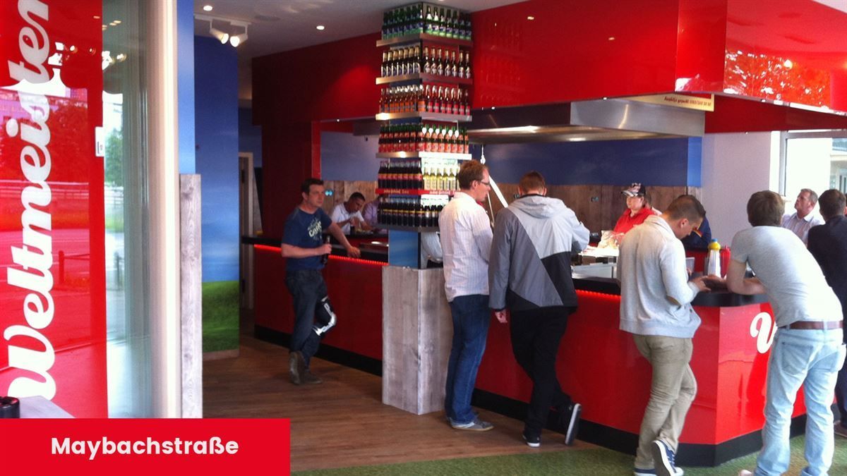 Eine Gruppe von Menschen steht an einem Tresen vor einem Schild mit der Aufschrift „maybachatrabe“