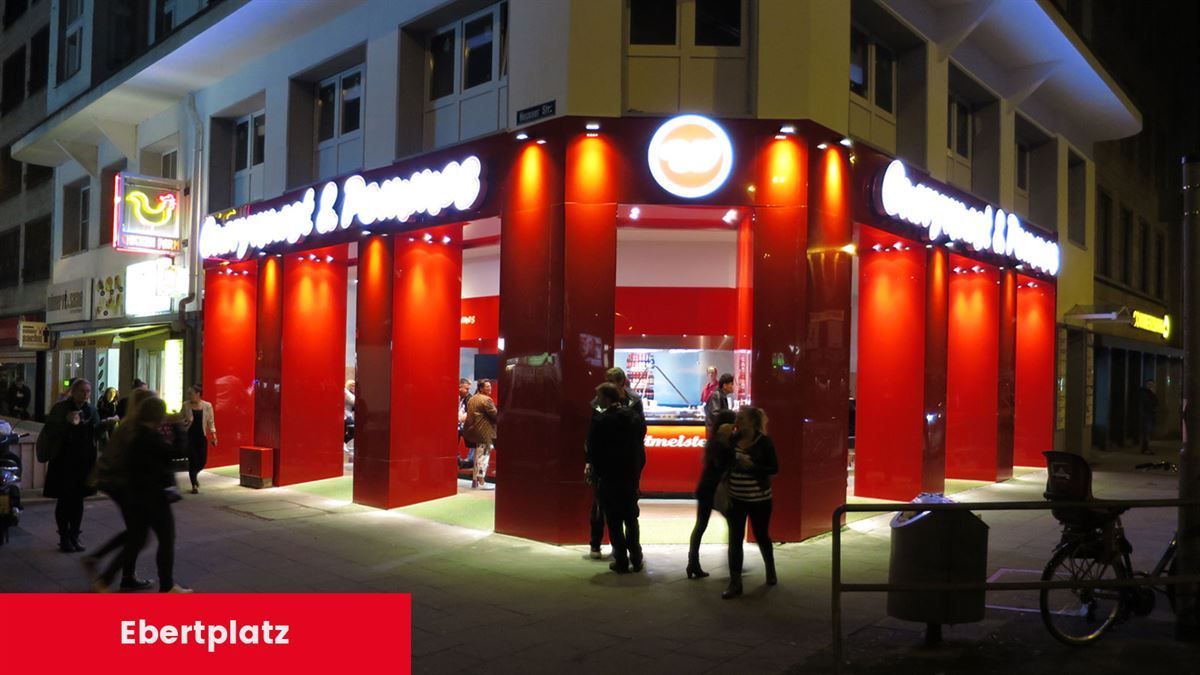 Eine Gruppe von Menschen steht vor einem Gebäude mit der Aufschrift „Ebertplatz“