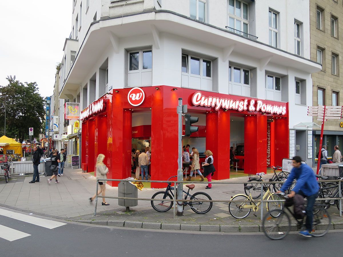 Ein Mann fährt Fahrrad vor einem Restaurant namens Currywurst & Pommes