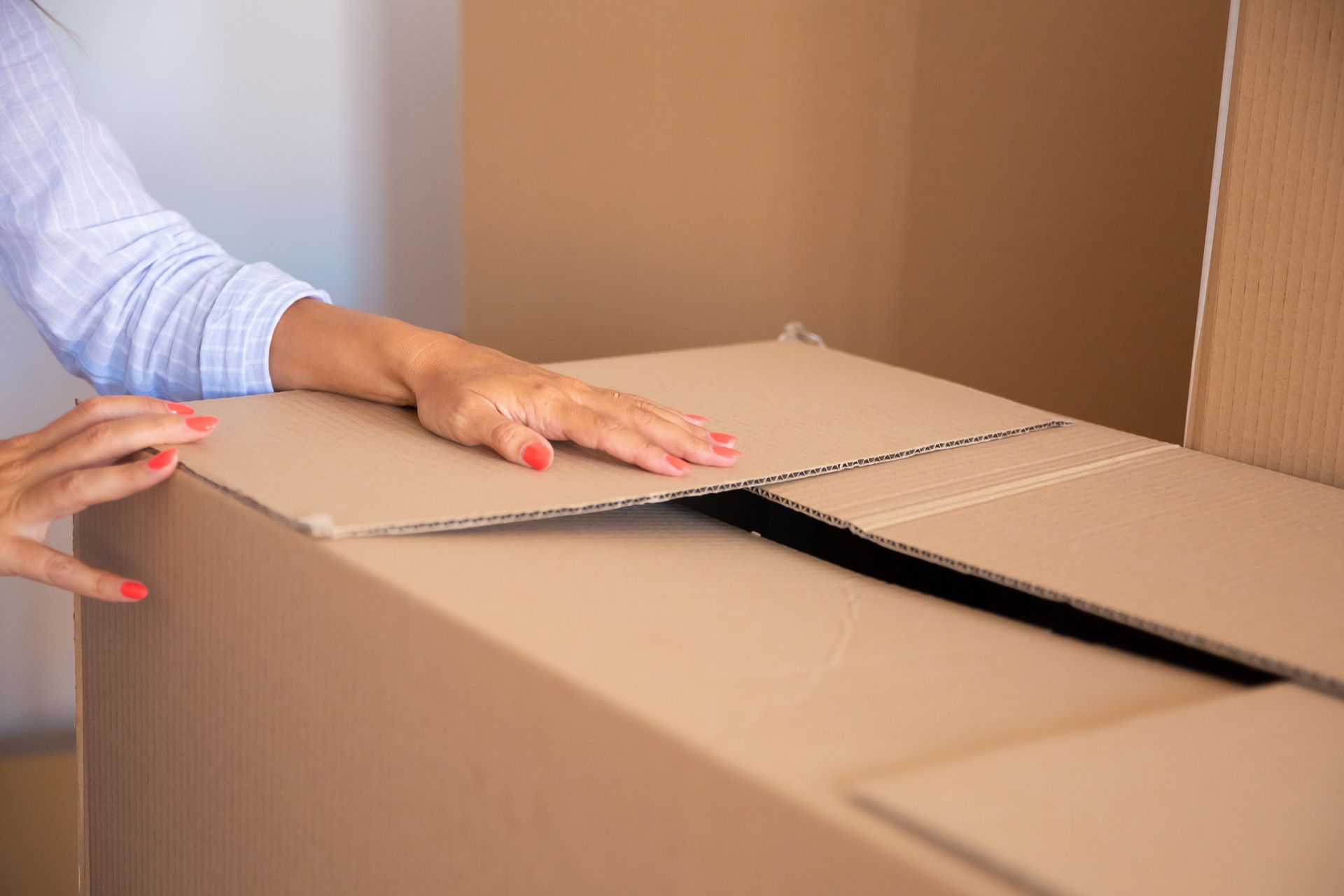 Mano cerrando las solapas de una gran caja de cartón en una habitación.