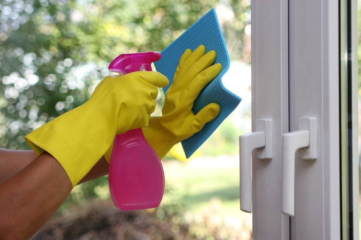 Una persona que lleva guantes amarillos está limpiando una ventana con una esponja y una botella de spray.