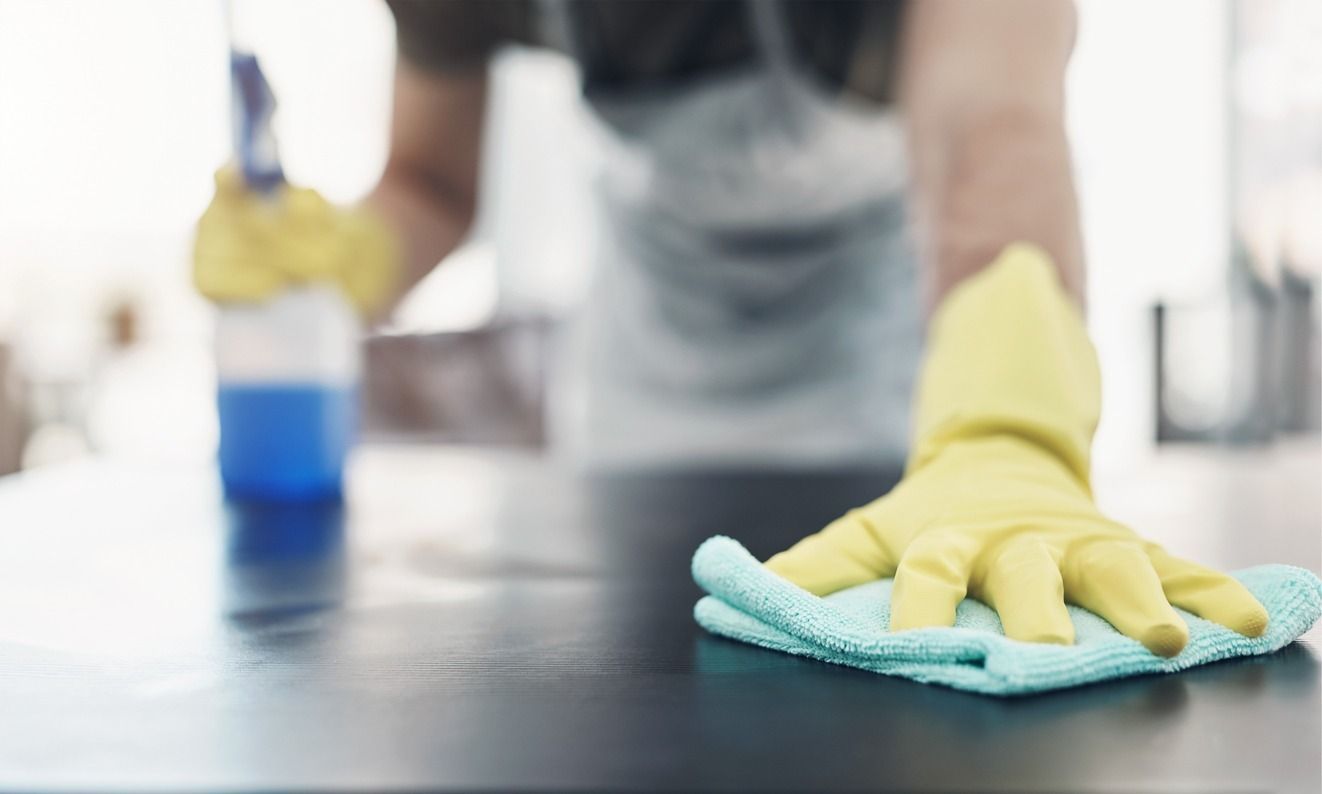 Una persona que lleva guantes amarillos está limpiando una mesa con un paño.