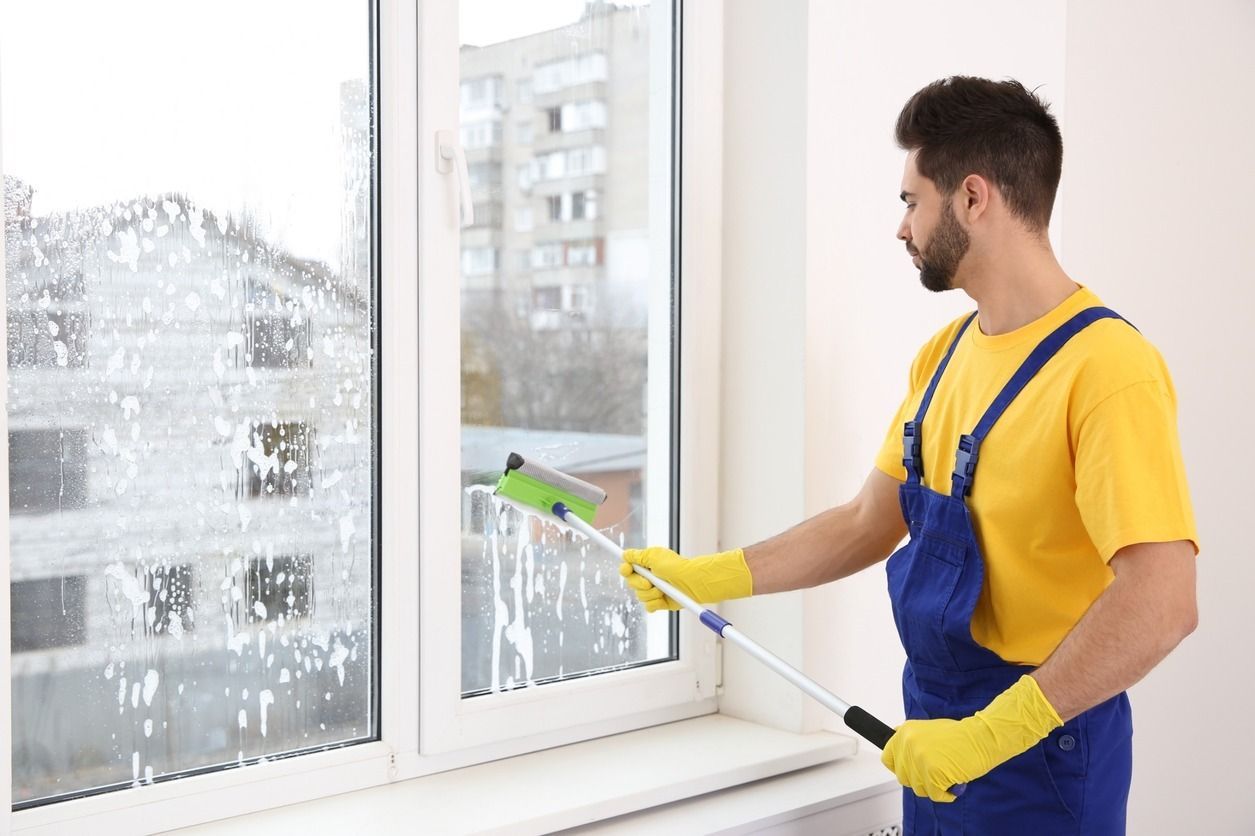 Un hombre está limpiando una ventana con un trapeador.