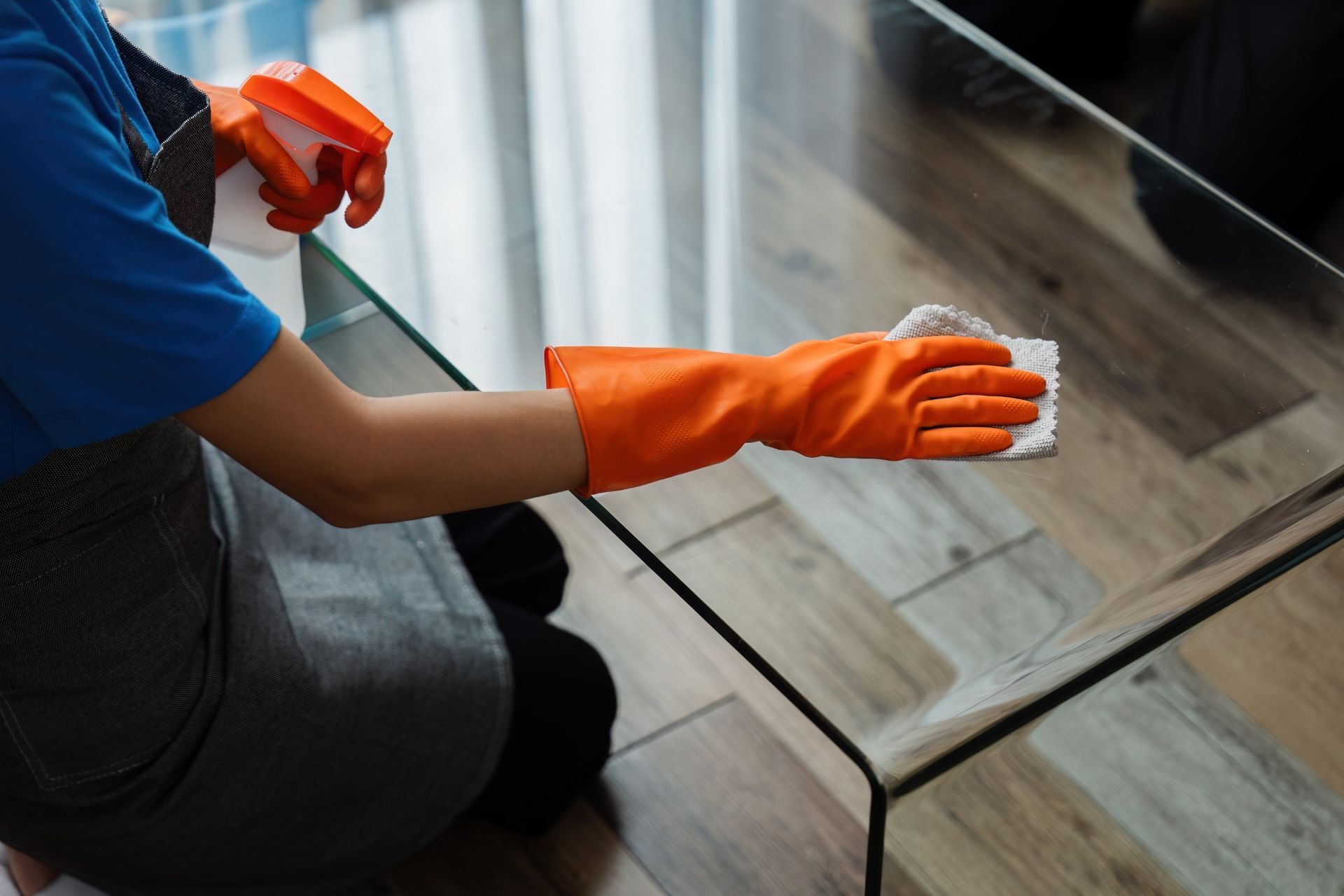 Una persona que lleva guantes naranjas está limpiando una mesa de cristal.