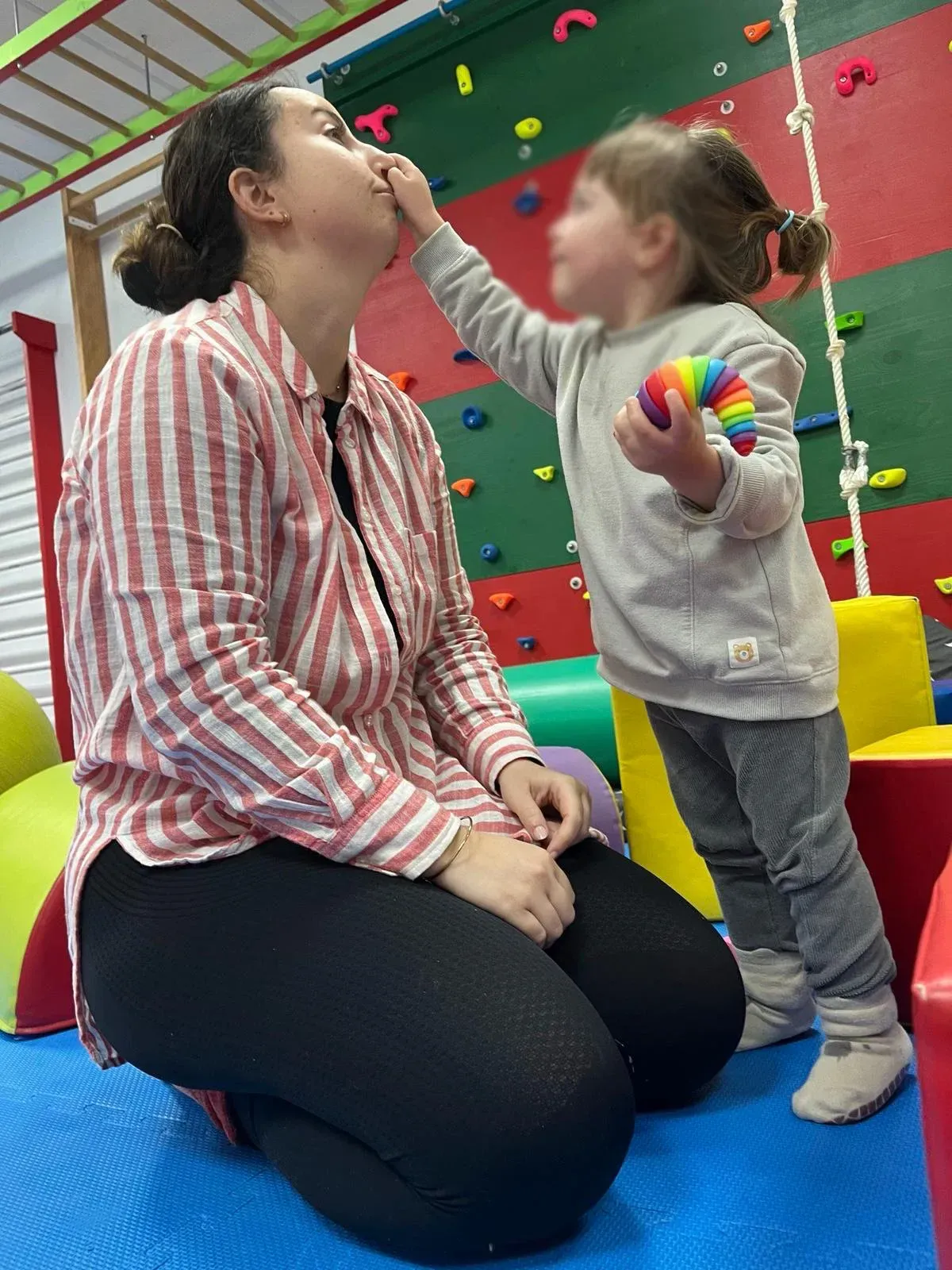 Una mujer está arrodillada junto a una niña que sostiene una pelota de arcoíris.