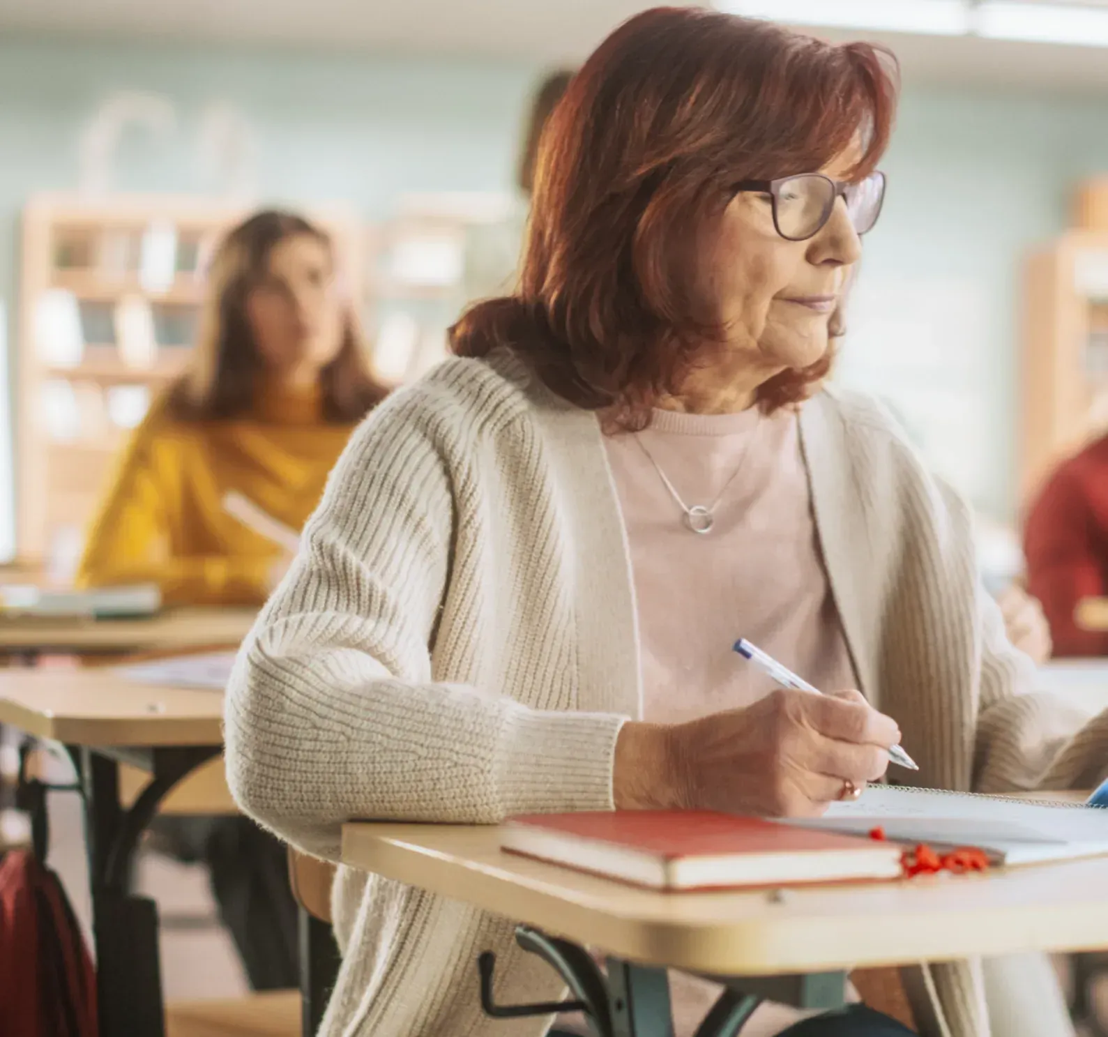 Una mujer está sentada en un escritorio en un aula escribiendo en un cuaderno.