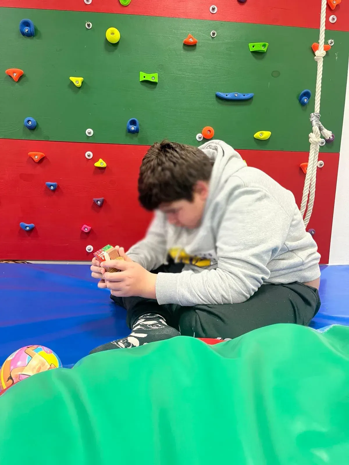 Un niño pequeño está sentado frente a un muro de escalada.