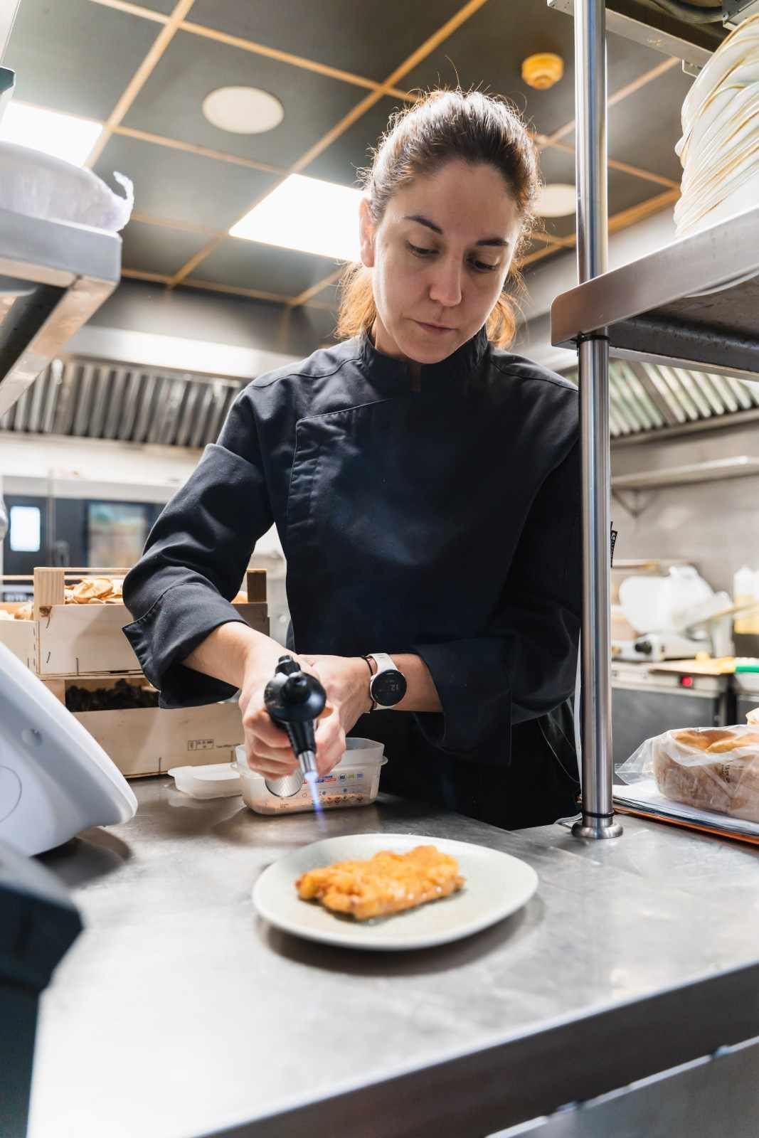 Chef quemando un plato empanizado en una cocina de acero inoxidable.