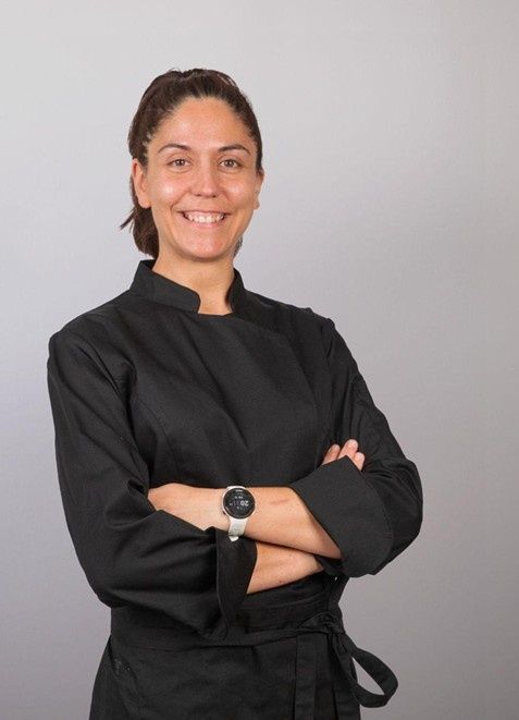 Mujer con chaqueta de cocinero negra, con los brazos cruzados, sonriendo.