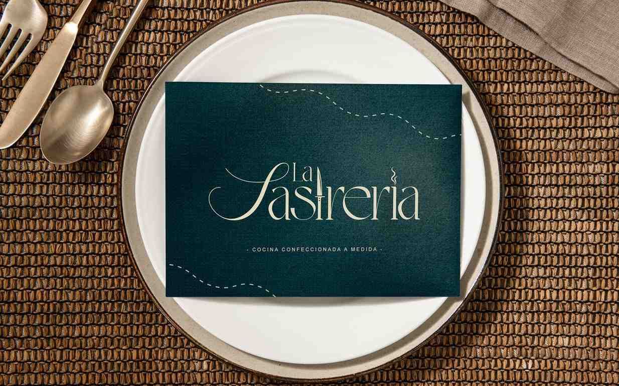 Una tarjeta de menú en un plato blanco con cubiertos. La tarjeta es verde azulado con letras doradas.