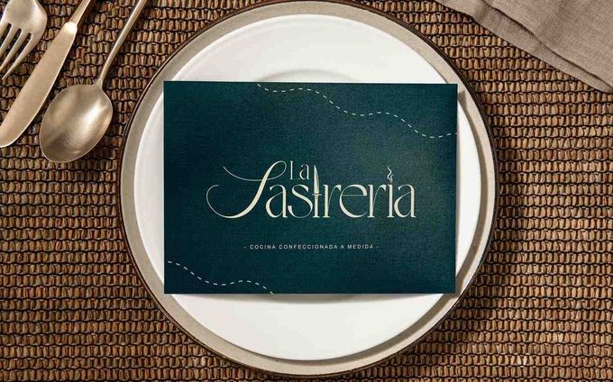 Una tarjeta de menú en un plato blanco con cubiertos. La tarjeta es verde azulado con letras doradas.