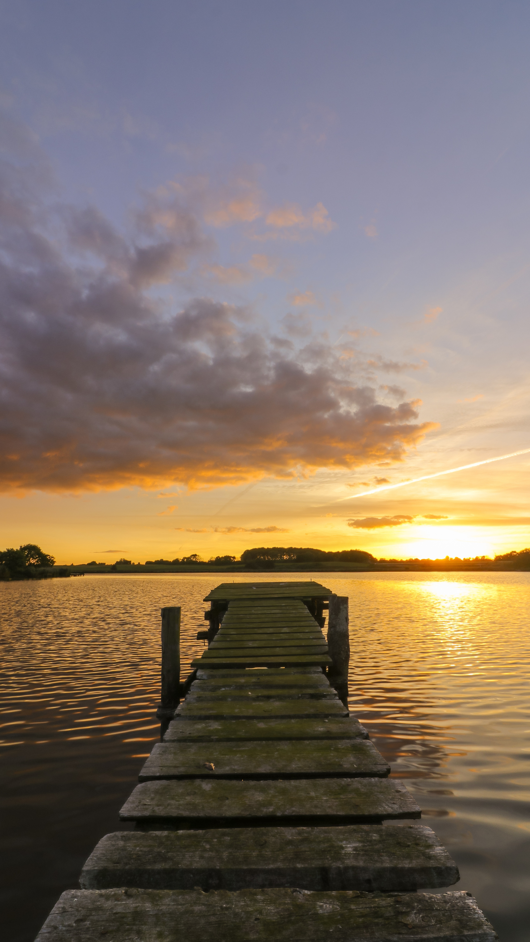Jetée en bois s'avançant dans un lac calme au coucher du soleil ; ciel orange et violet se reflétant sur l'eau.