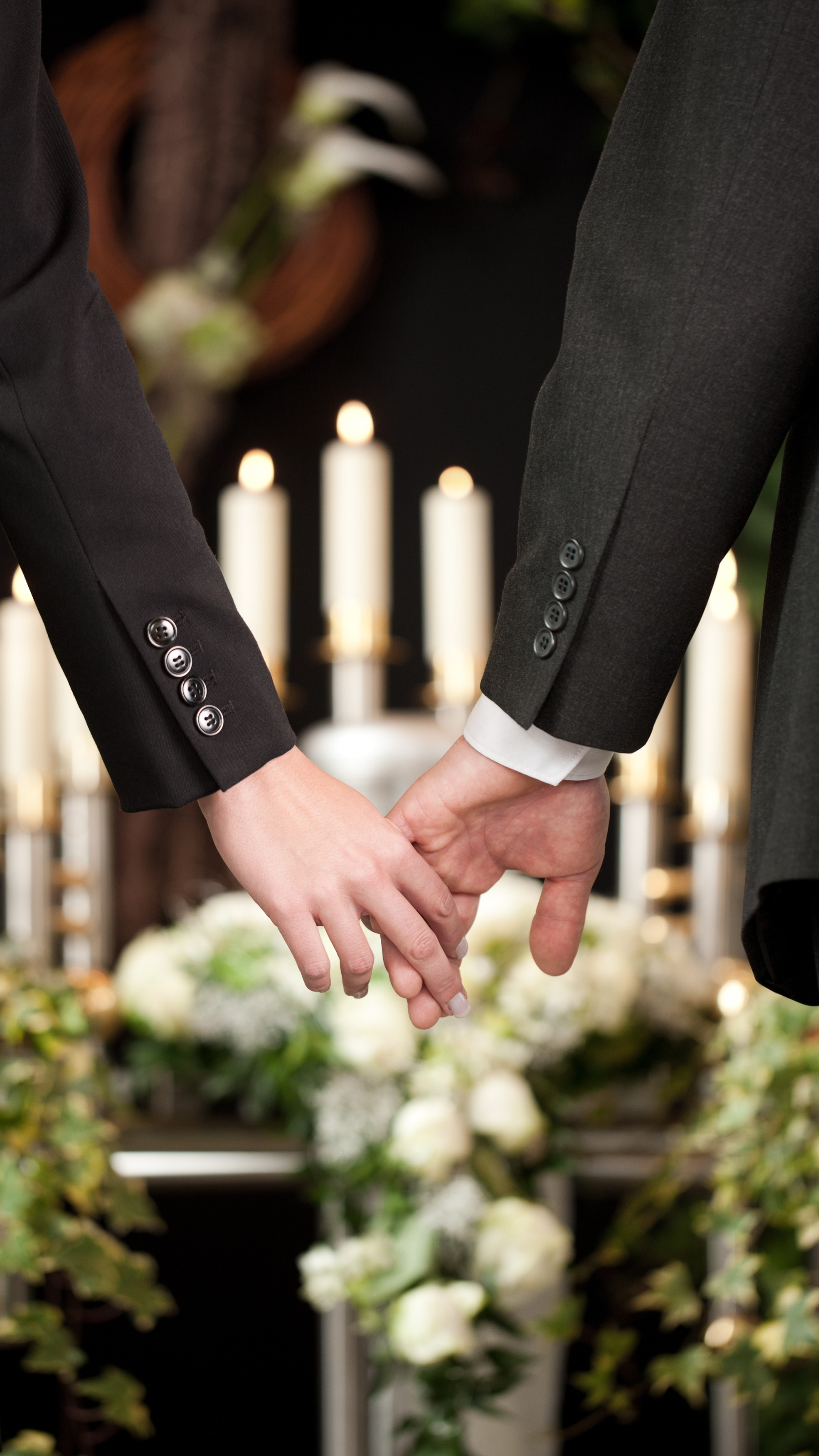 Deux personnes se tiennent la main, entourées de fleurs et de bougies.