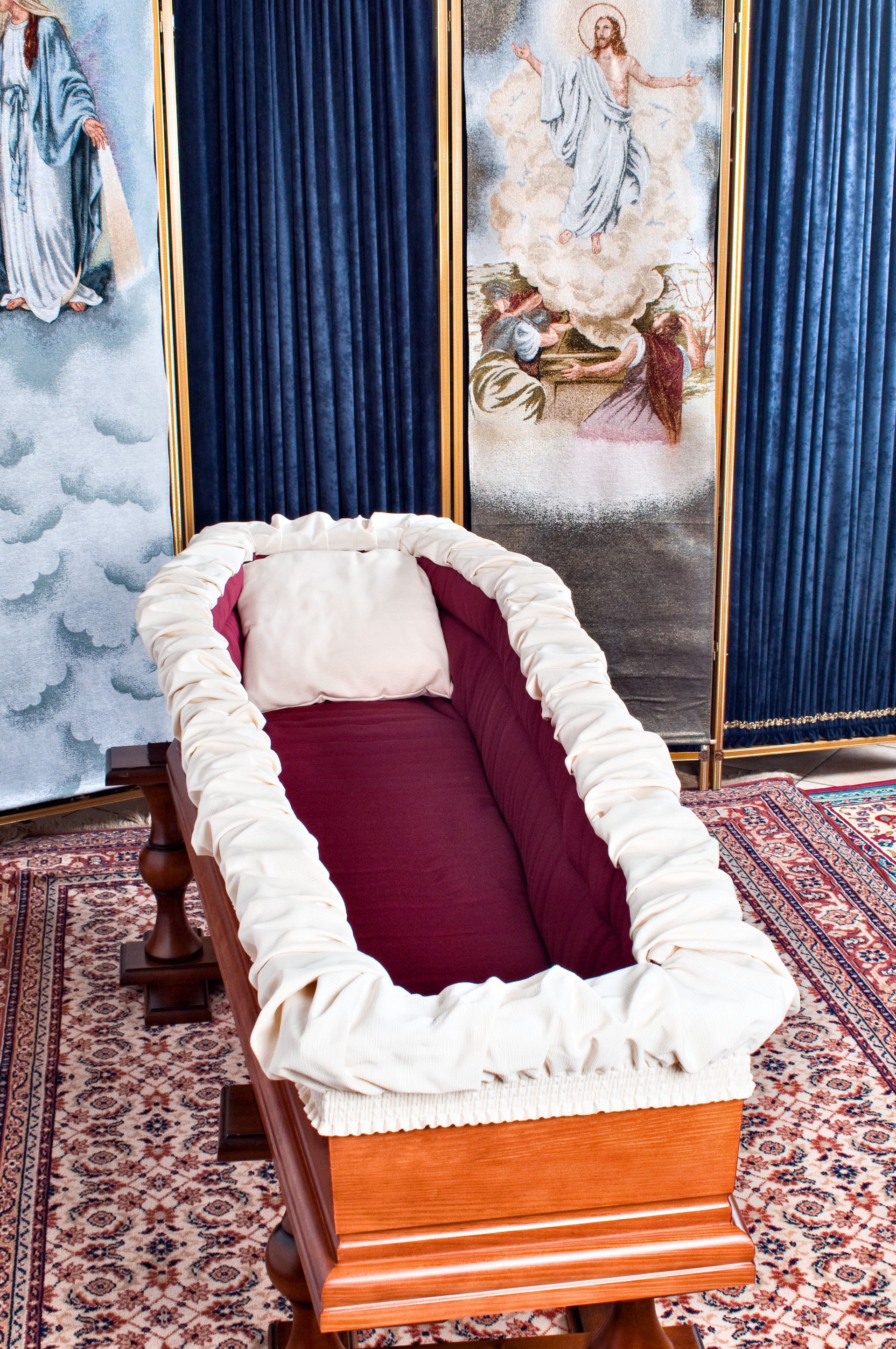 Cercueil en bois doublé de blanc avec oreiller, placé sur un support.