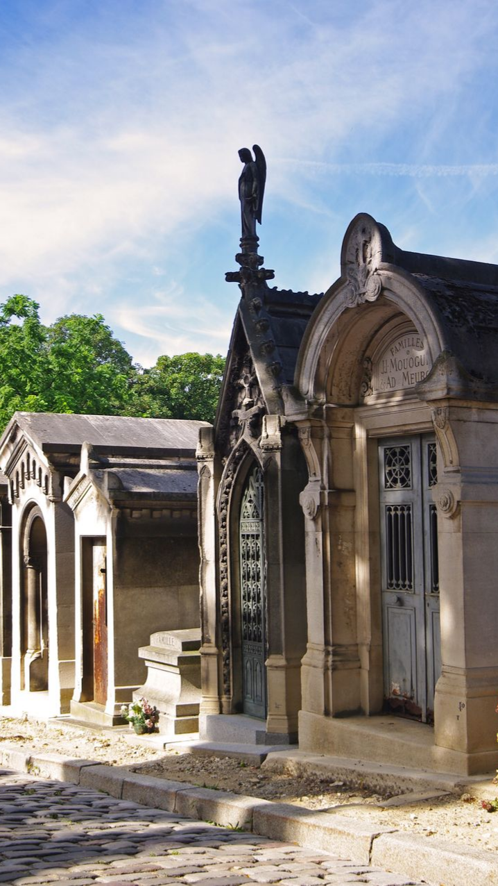 Mausolées de pierre dans un cimetière aux détails ornementaux, un ciel au-dessus et une statue d'ange.