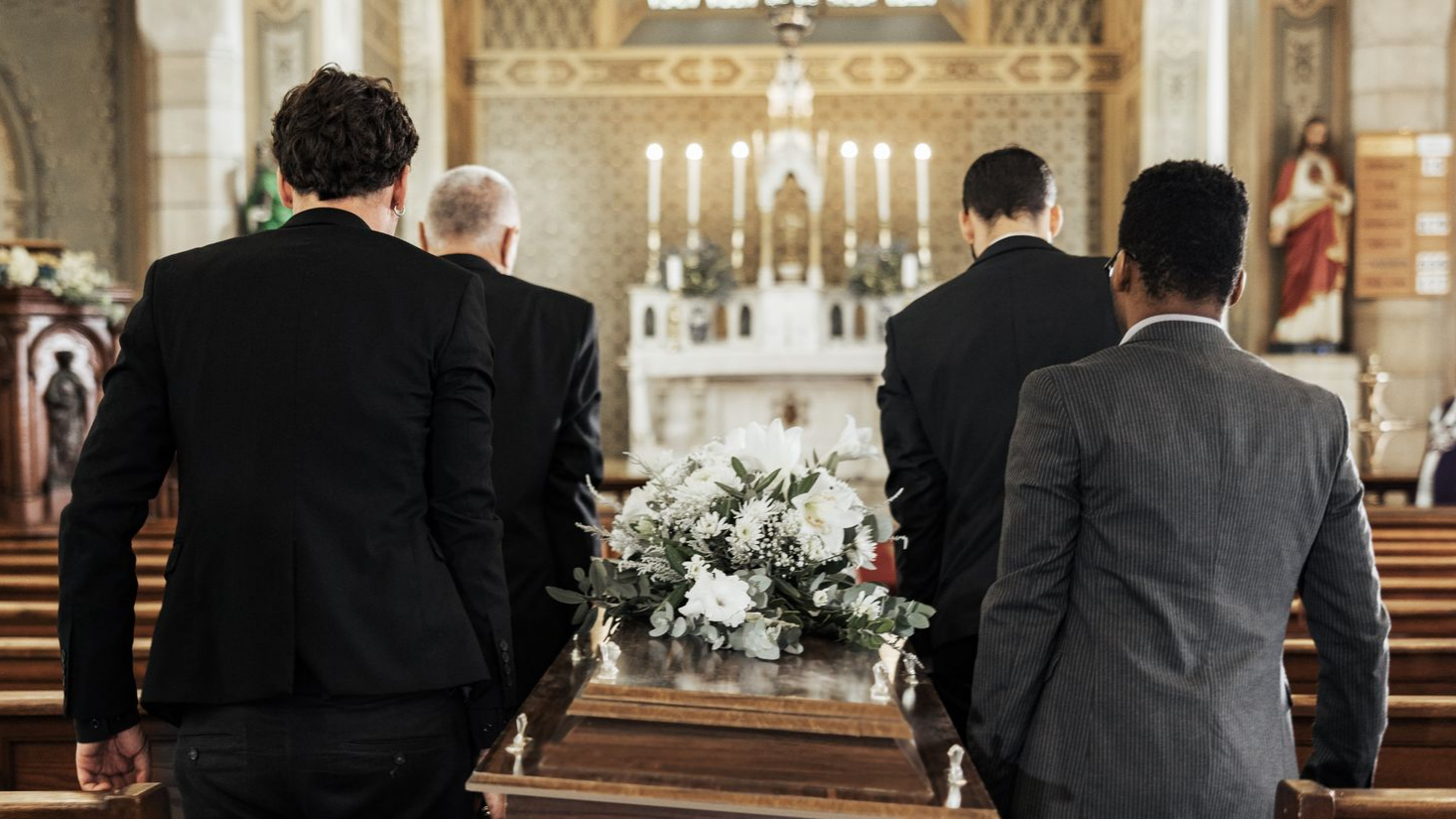 Des porteurs transportent un cercueil orné de fleurs blanches dans une église.