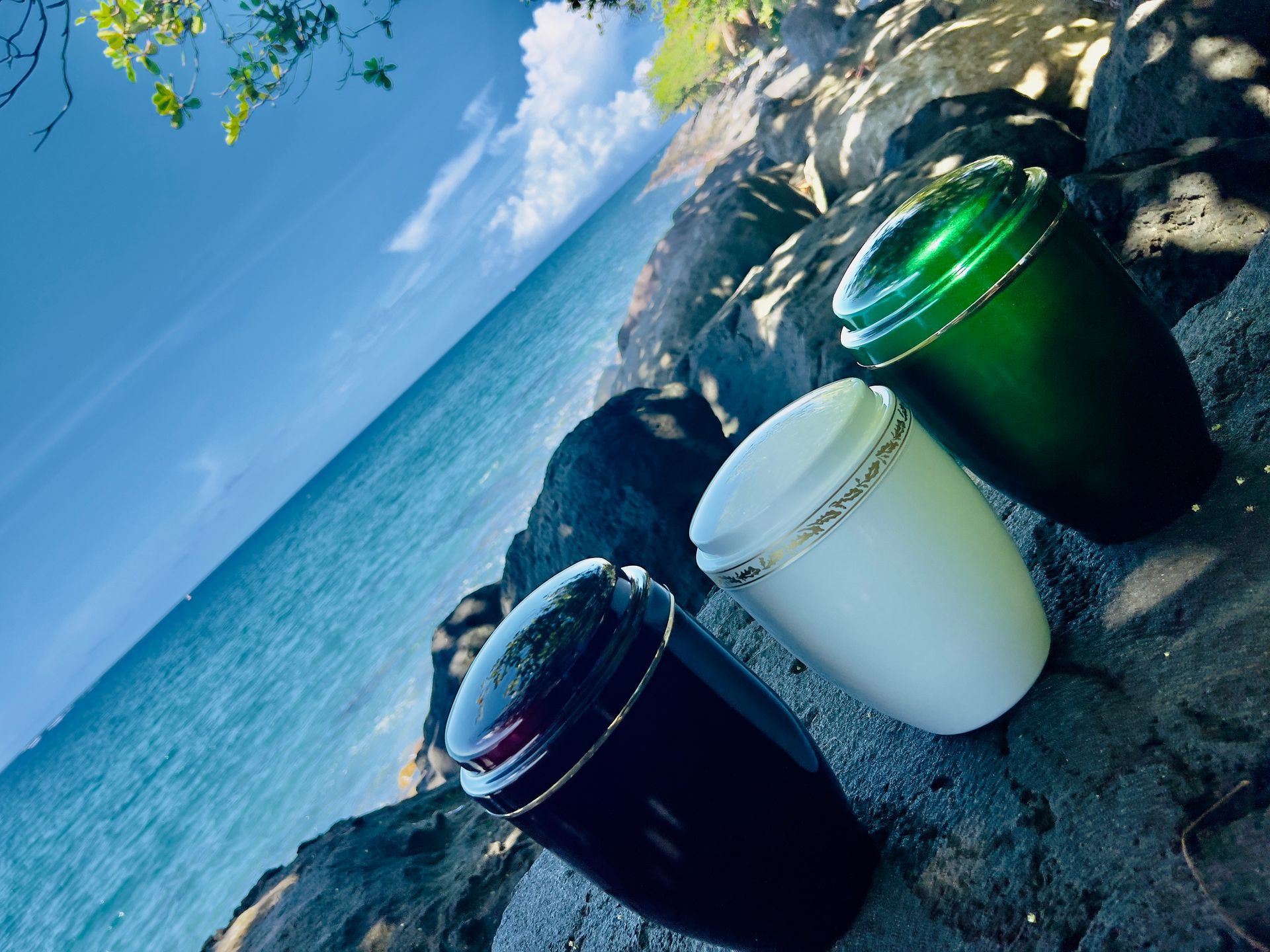 Trois urnes colorées sur des rochers, océan et ciel bleu en arrière-plan.