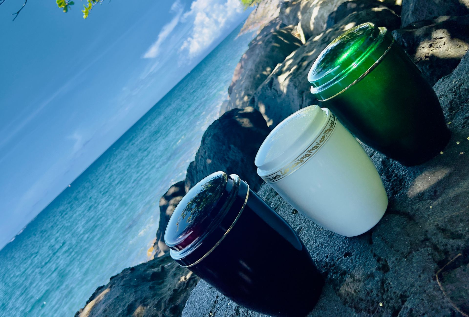 Trois urnes colorées sur des rochers, avec l'océan et le ciel en arrière-plan.