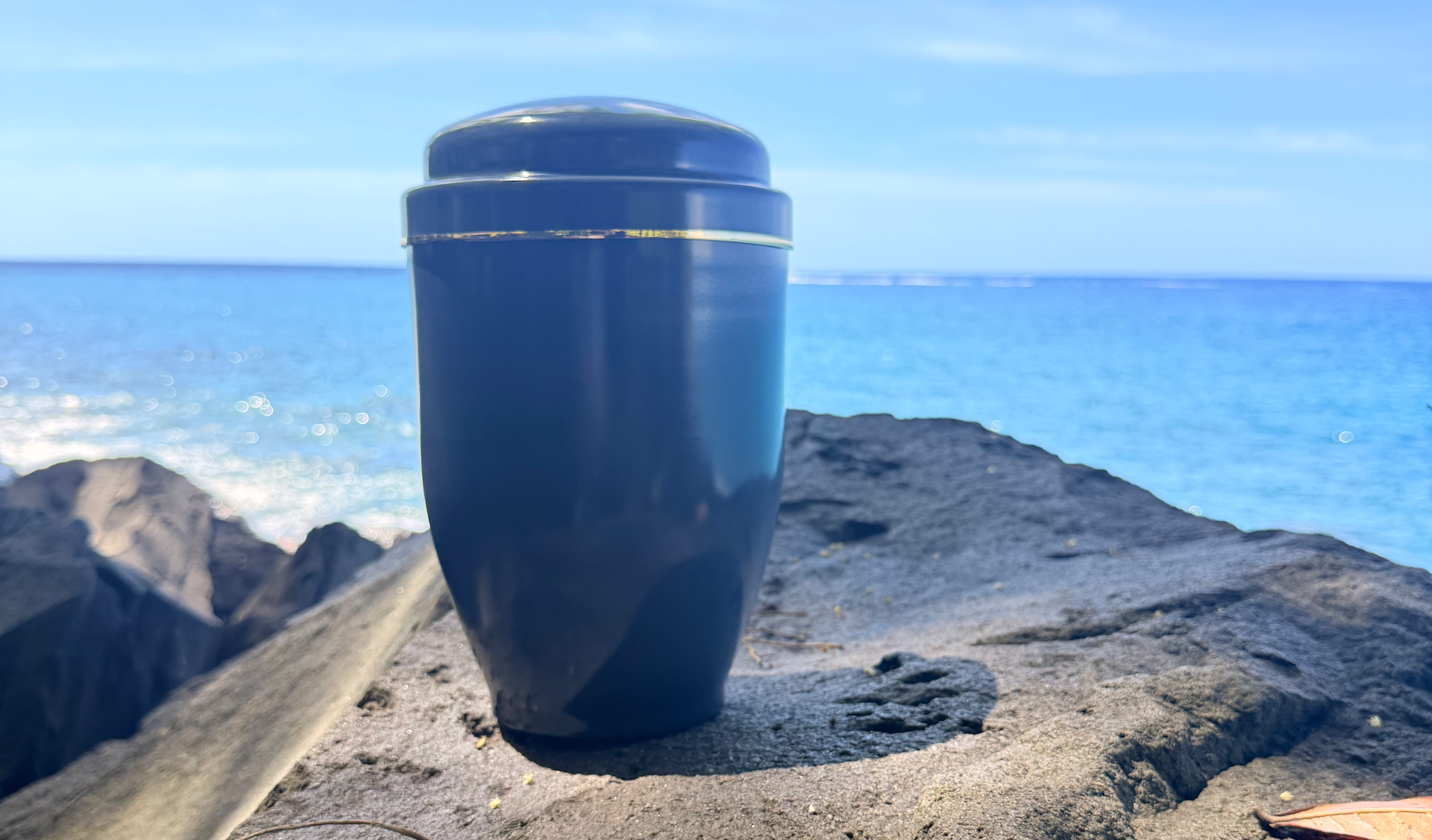 Urne bleue posée sur un rocher, avec l'océan et le ciel bleu en arrière-plan.
