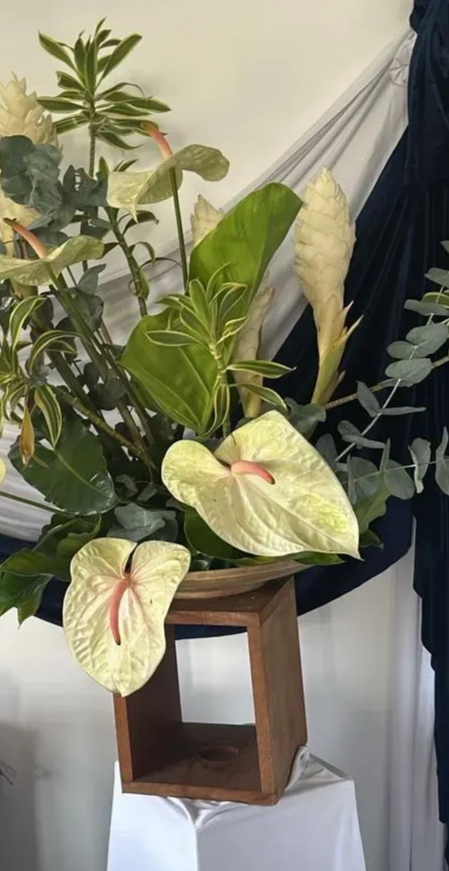 Composition florale de fleurs blanches et vertes dans un cube en bois, sur fond de tissu blanc et bleu marine.