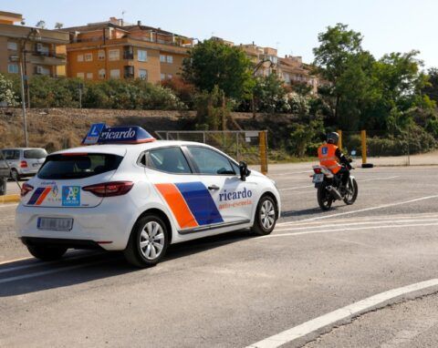 Coche y moto en un examen de conducir. Coche blanco con instructor y motociclista con chaleco naranja.