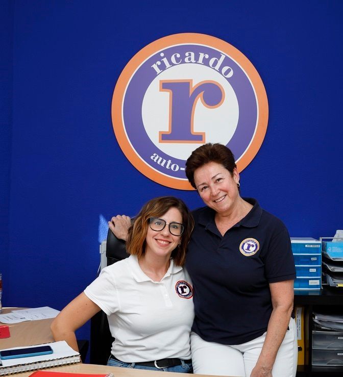 Mujer en el escritorio sonriendo, detrás de una computadora, fondo de oficina con logotipos.
