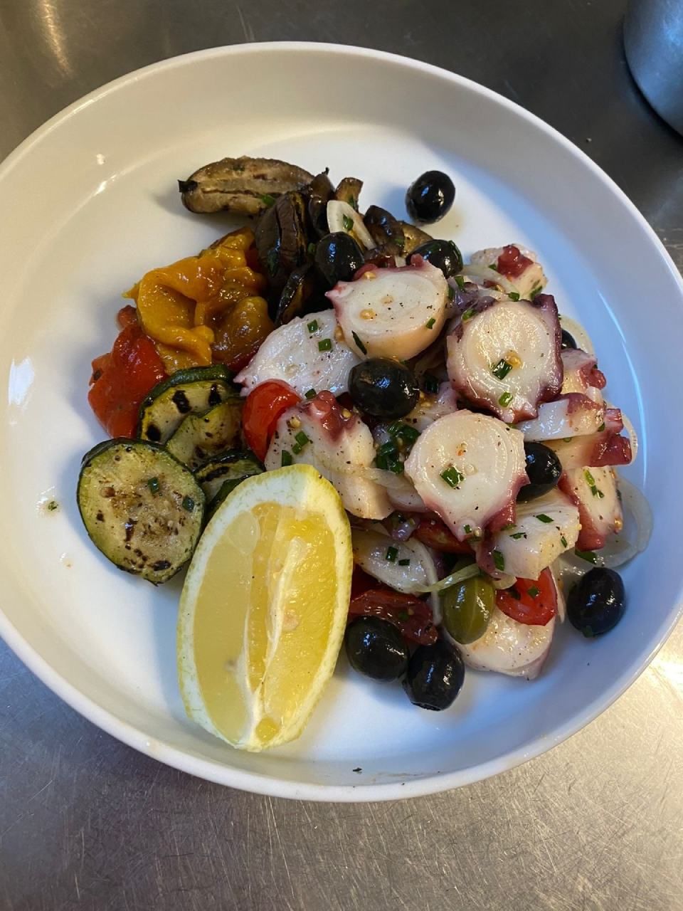 Une assiette blanche garnie de légumes de poulpe et d'une tranche de citron
