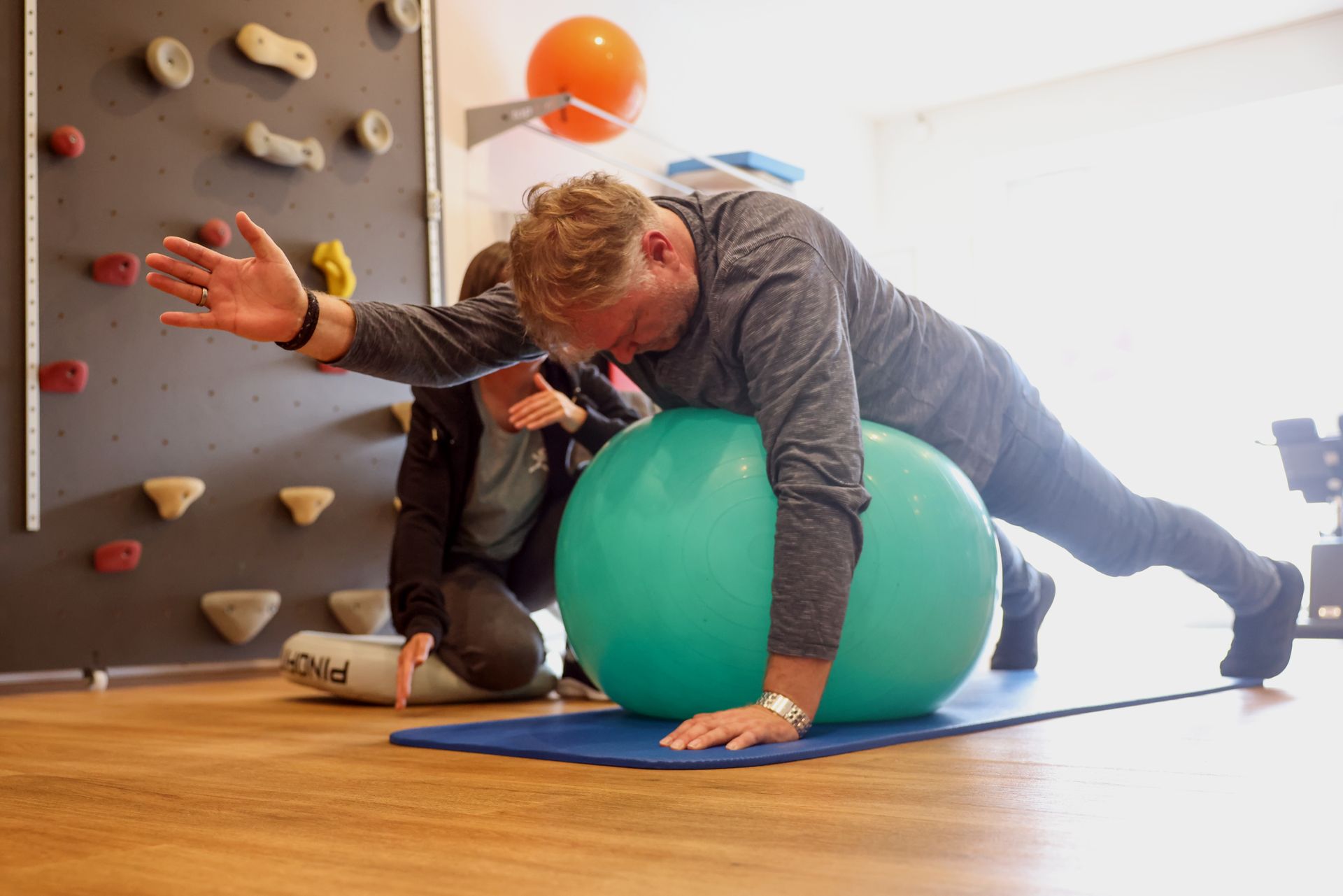 Eine Person liegt zur Therapie auf einem großen grünen Gymnastikball, während eine andere Person sie anleitet
