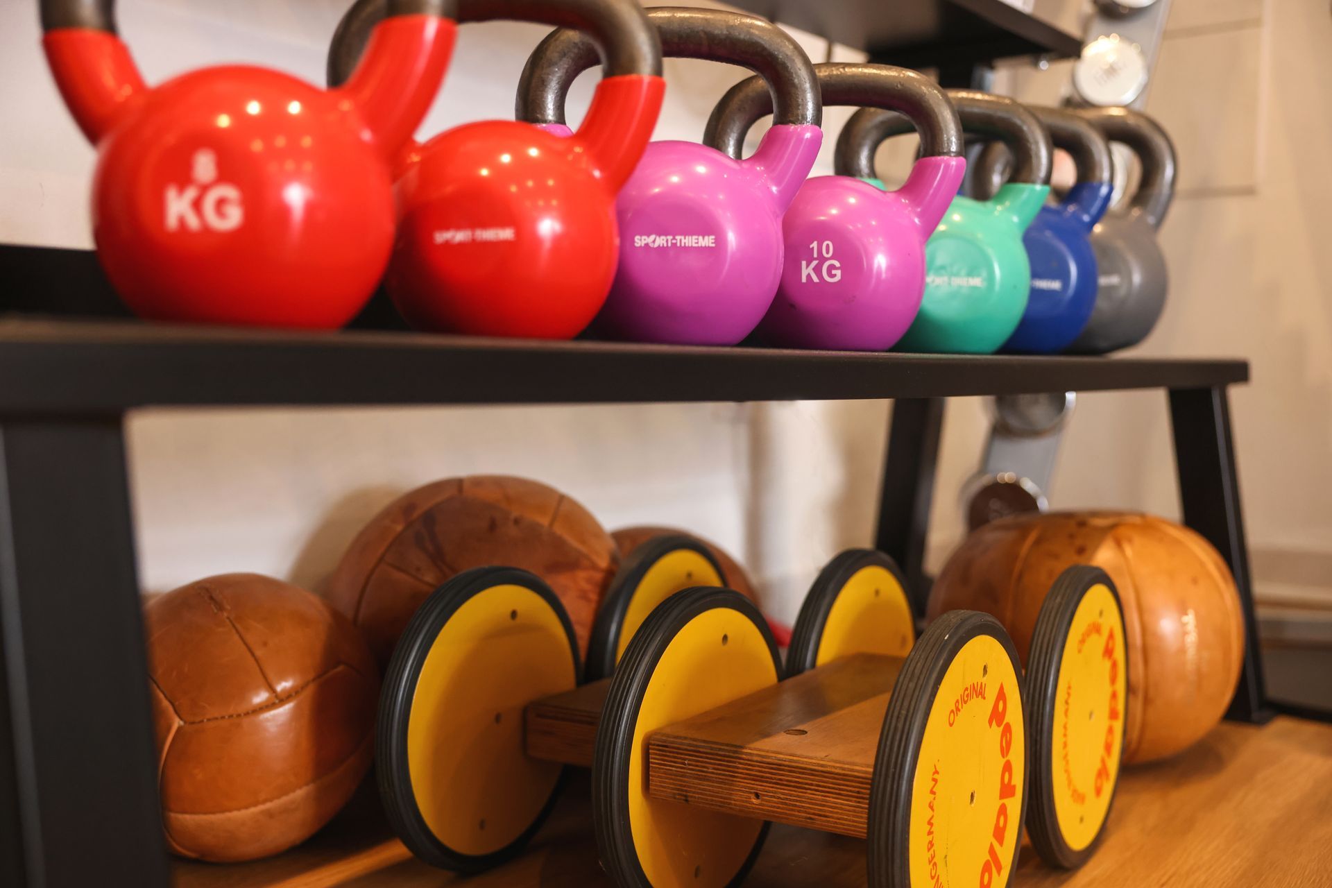 Bunte Kettlebells und Gewichtsscheiben stehen ordentlich auf einem Regal in einem Trainingsraum.