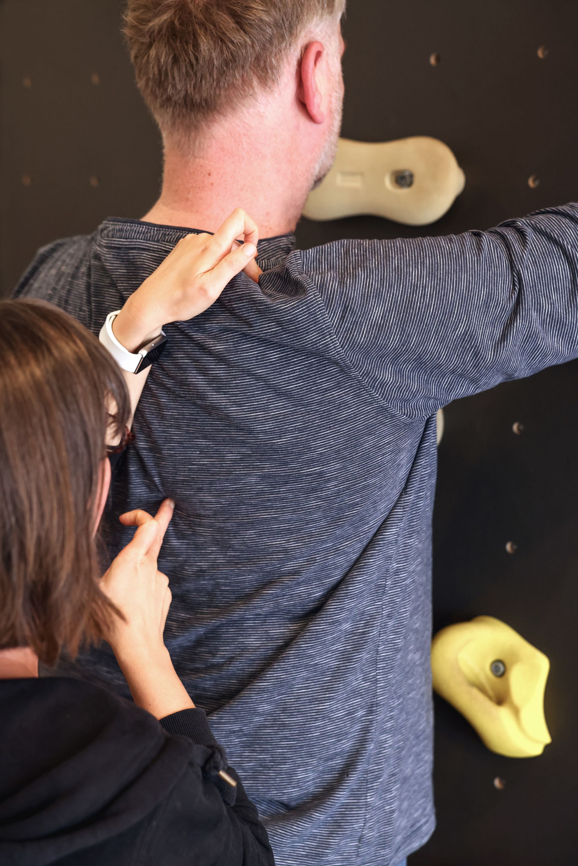 Therapeutin greift sanft an die Schulter einer Person, die vor einer Kletterwand steht.