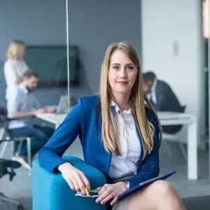 Une femme portant une veste bleue est assise sur une chaise et tient un presse-papiers.