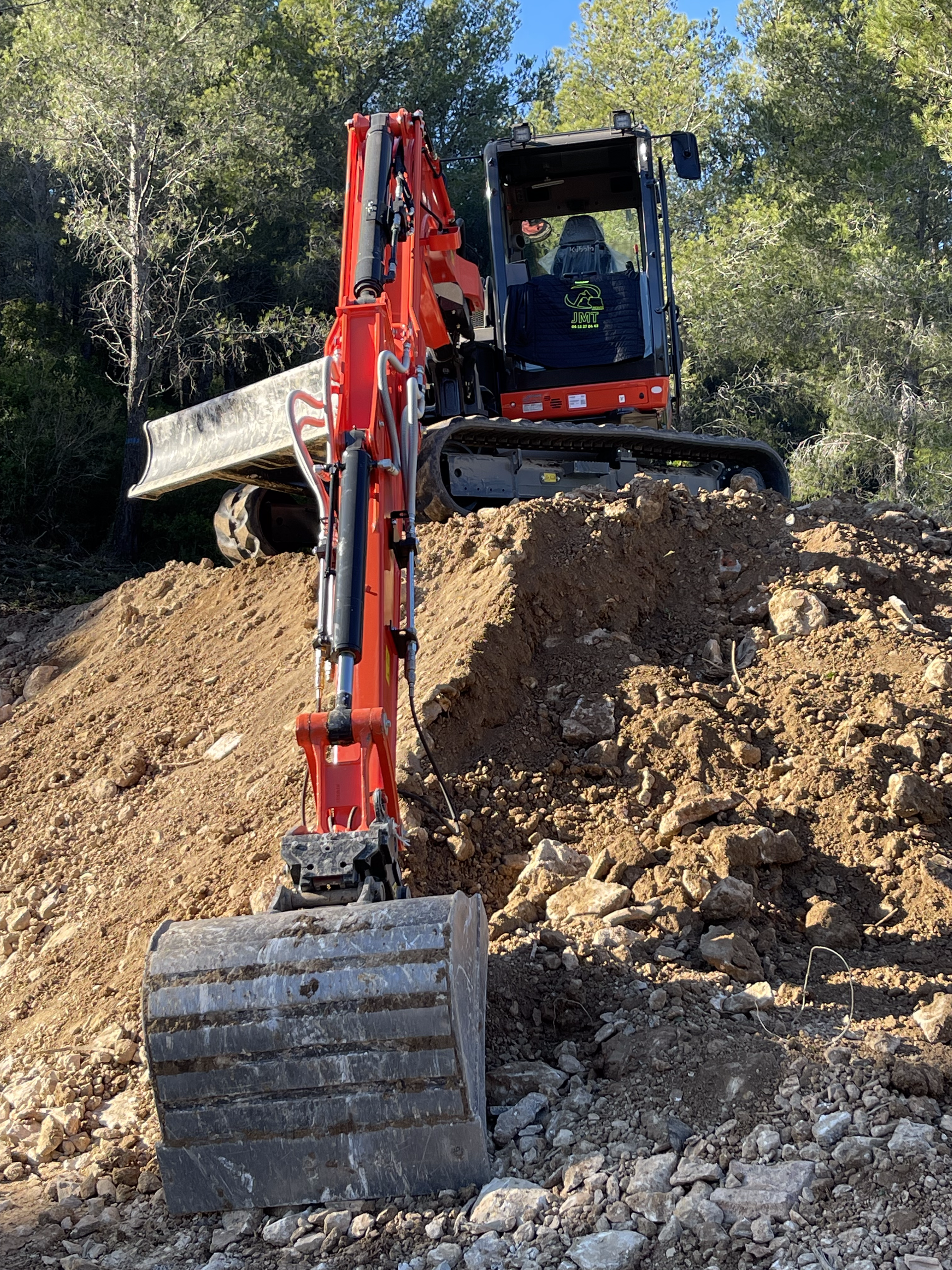Une excavatrice rouge déplace de la terre sur un tas de rochers.