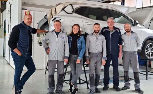 Bureau d'accueil dans un cabinet médical avec un ordinateur, un téléphone et une salle d'attente visibles à travers une porte vitrée.