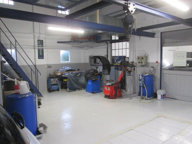 Intérieur du garage : sol blanc, équipement bleu, monte-voiture noir, murs gris, outils et un escalier.